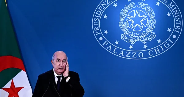 Un responsable au pupitre lors d'une conférence de presse, sous les couleurs algériennes à Rome.