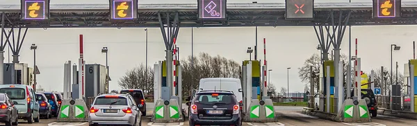 Barrières de péage rouges et blanches avec feux de signalisation et voitures en attente, vue en angle plongeant.