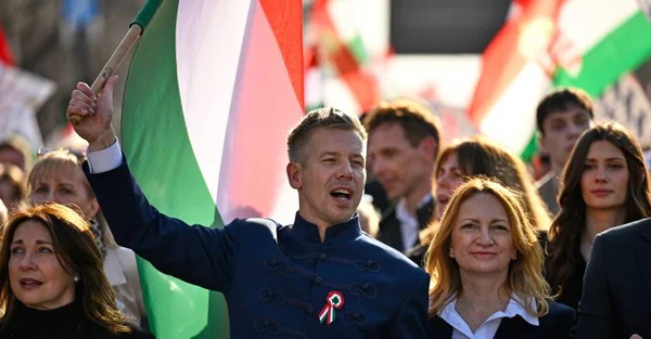 Péter Magyar au milieu d'une foule, portant une veste traditionnelle et tenant un drapeau en l'air.