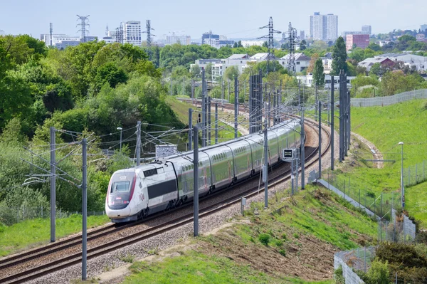 Un TGV circulant sur une voie courbée entourée de verdure et d'infrastructures urbaines.