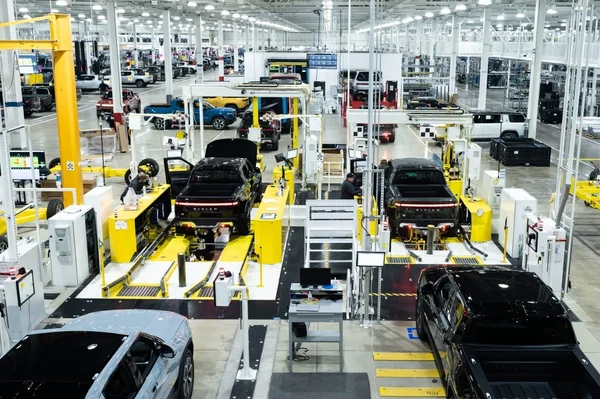 Chaîne d'assemblage de l'usine Rivian, avec des camionnettes électriques noires et des robots industriels.