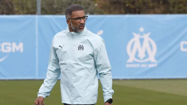 Habib Beye, entraîneur de l'OM, exprimant son mécontentement devant un mur de logos.