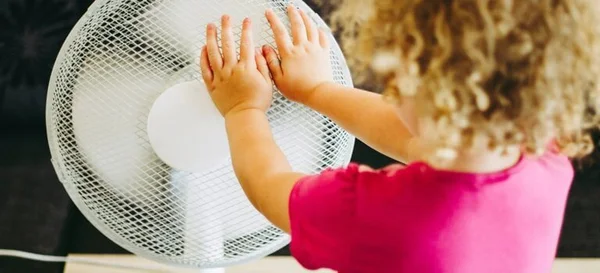 Enfant touchant la grille d'un ventilateur pour se rafraîchir pendant la canicule.