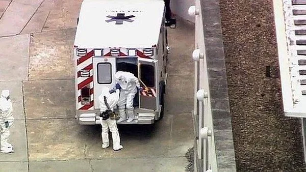 Ambulance avec personnel en combinaison Hazmat s’occupant d’un patient sur brancard.