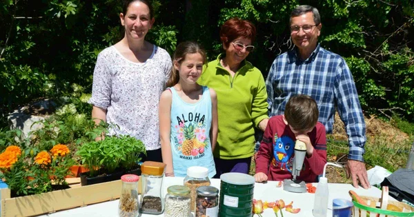 Famille réunie autour d'une table de jardin avec des graines et un microscope, dans une pépinière à Orange.