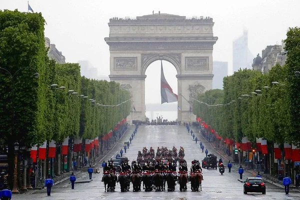 Cavaliers de la Garde républicaine sur les Champs-Élysées lors de la cérémonie du 8-Mai, avec le drapeau français dans l'Arc de Triomphe.
