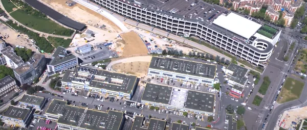 Vue aérienne du chantier du CDG Express avec un parking à étages et un centre commercial à proximité.