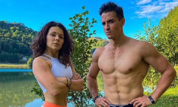Tibo InShape et Juju Fitcats posant ensemble devant un paysage naturel avec un lac.