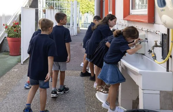 Des écoliers se lavent les mains dans une cour d'école, une mesure d'hygiène renforcée pendant la canicule.