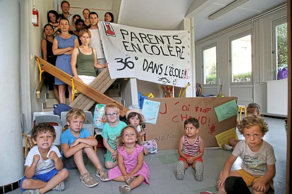 Parents et élèves manifestent contre la chaleur dans une école, pancartes à la main.