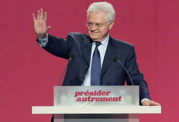 Lionel Jospin derrière un pupitre de campagne, agitant la main.
