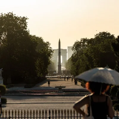 Paris sous la chaleur : une femme se protège du soleil avec un parapluie devant l'obélisque de la Concorde.