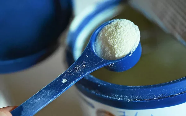 Cuillère doseuse de lait en poudre au-dessus d'un contenant.
