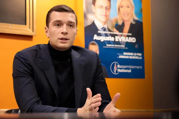 Jordan Bardella lors d'une interview, devant une affiche du Rassemblement National.