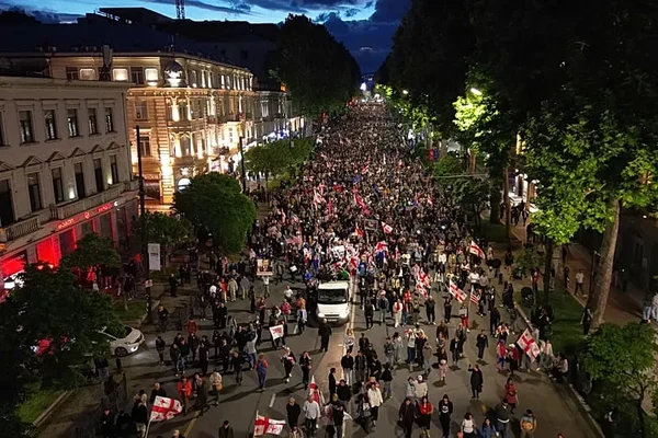 Défilé massif pro-UE sur une grande avenue de Tbilissi, avec des bâtiments historiques illuminés en arrière-plan.