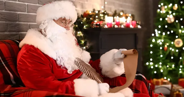 Père Noël lisant un parchemin dans un décor de Noël avec sapin et cheminée.