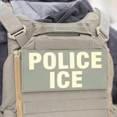 Écusson 'POLICE ICE' sur le gilet tactique d'un agent.