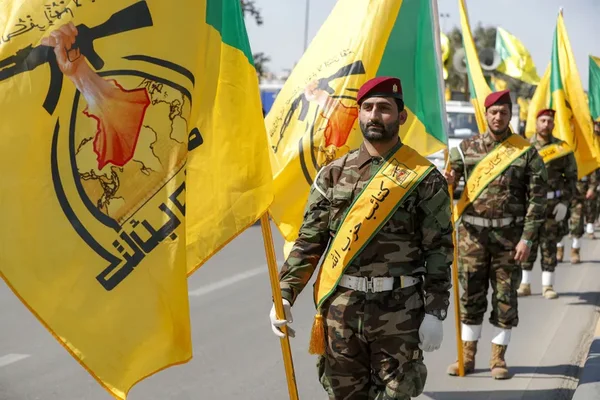 Membres de la milice pro-iranienne Ashab Al-Kahf défilant avec leurs drapeaux jaunes.