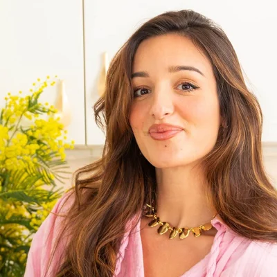 Loulou Kitchen, influenceuse, affichant une expression espiègle devant une armoire blanche et des fleurs jaunes.
