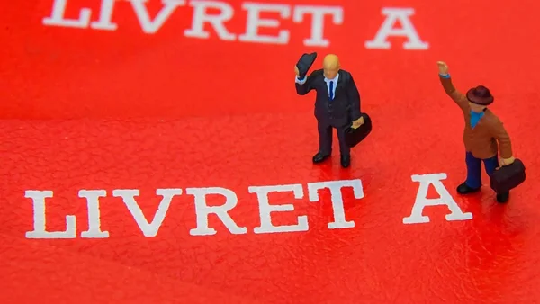 Deux figurines en costume sur un livret A, symbolisant le financement des nouveaux réacteurs EPR 2.