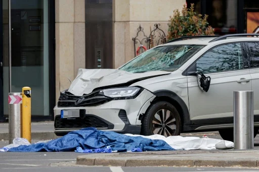 Une voiture argentée endommagée et une bâche recouvrant une personne au sol à Leipzig.