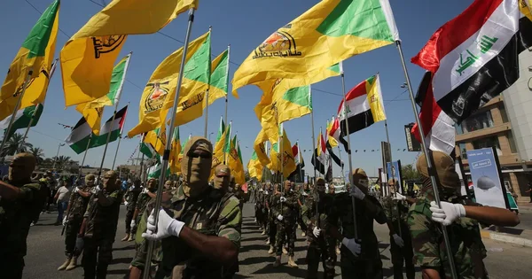 Membres des Kataeb Hezbollah lors d'un défilé militaire en Irak, arborant des drapeaux jaunes et irakiens.