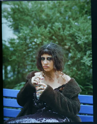 Gildaa, vêtue d'un manteau en fourrure et d'une robe à sequins, assise sur un banc.