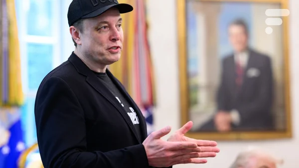 Elon Musk s'exprime lors d'un événement, avec un portrait en arrière-plan.