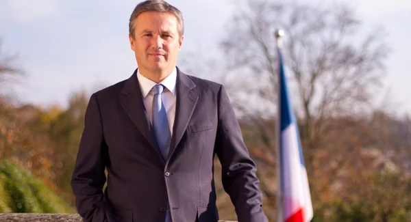 Nicolas Dupont-Aignan posant devant un drapeau français.