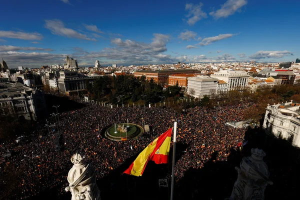 Des dizaines de milliers de manifestants rassemblés à Madrid, avec un drapeau espagnol au premier plan.