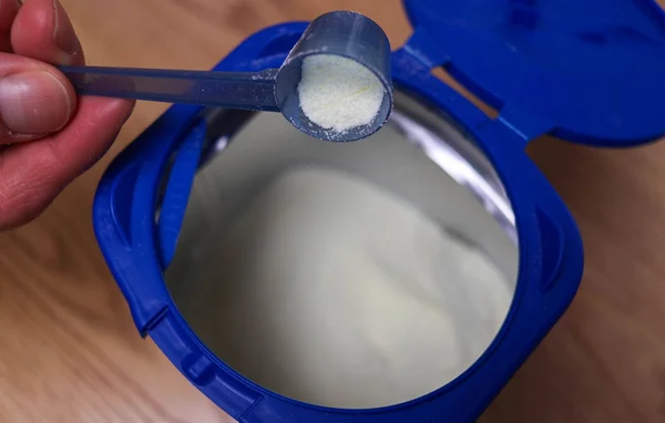 Cuillère doseuse de lait infantile en poudre au-dessus d'une boîte ouverte.