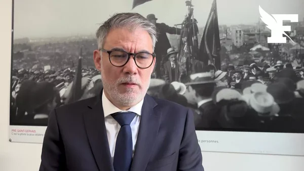 Jean-Luc Mélenchon s'exprimant lors d'un hommage, devant une photographie de foule.