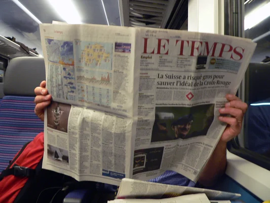 Un lecteur parcourt Le Temps dans un train, démontrant la portée mobile du journal.