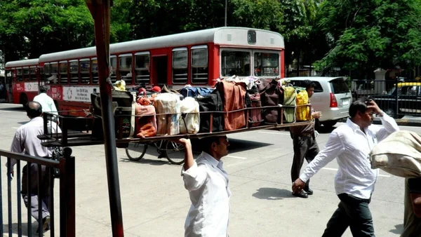 Un homme transporte des marchandises sur sa tête dans une rue animée en Inde, illustrant l'économie informelle de la livraison.