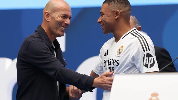 Michel Platini échangeant une poignée de main avec Kylian Mbappé en maillot du Real Madrid.