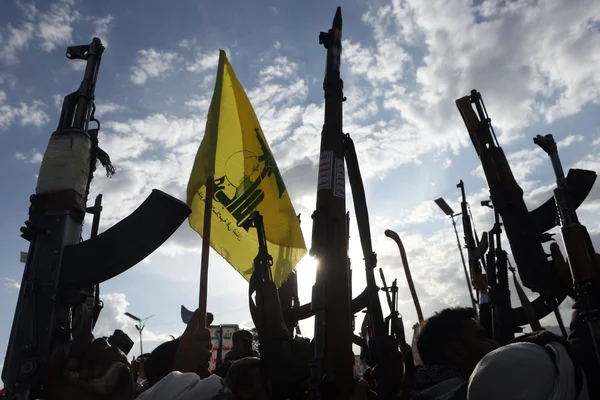 Foule de combattants houthis brandissant des armes et un drapeau jaune.