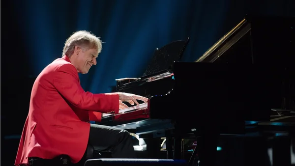 Richard Clayderman en concert, jouant sur scène sous un éclairage bleu.