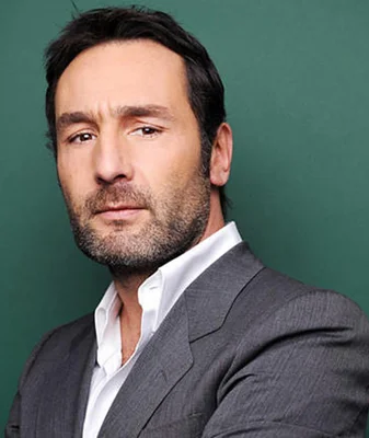 Gilles Lellouche en chemise blanche et veste grise, fond vert.