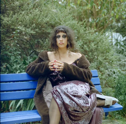 Portrait de Gildaa en tenue de scène, assise sur un banc de parc.