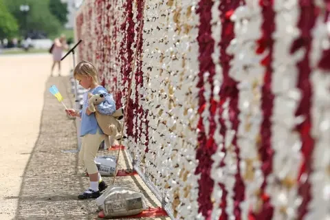 Un enfant tenant un drapeau ukrainien et un ours en peluche devant un mur de fleurs, lors des commémorations du Jour de la Victoire à Moscou.