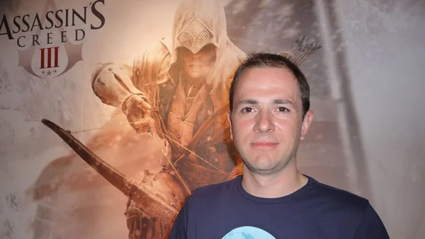 Alex Hutchinson, réalisateur de Far Cry 4, devant une affiche d'Assassin's Creed III.