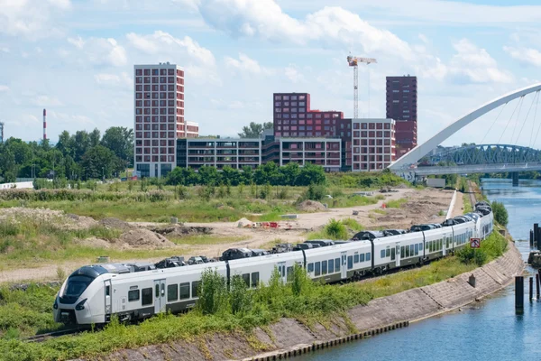 Le CDG Express en circulation sur une voie longeant un canal, avec des immeubles modernes en arrière-plan.