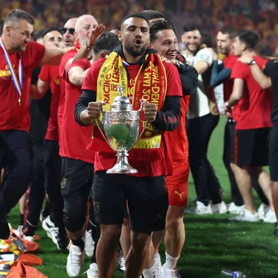 Un joueur du RC Lens brandit le trophée de la Coupe de France, entouré de coéquipiers en fête sur la pelouse.