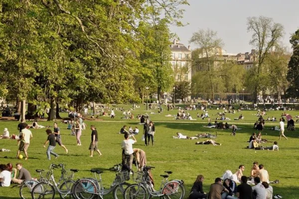 Un parc urbain animé un dimanche ensoleillé, avec des vélos et des promeneurs sur la pelouse.