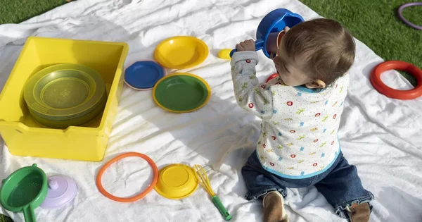 Un enfant jouant avec des jouets de cuisine en plastique sur une couverture blanche.