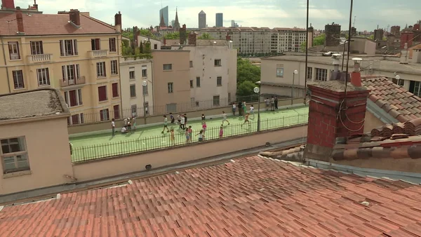 Enfants jouant sur une cour d'école végétalisée en toiture, avec vue sur Paris et la Défense.
