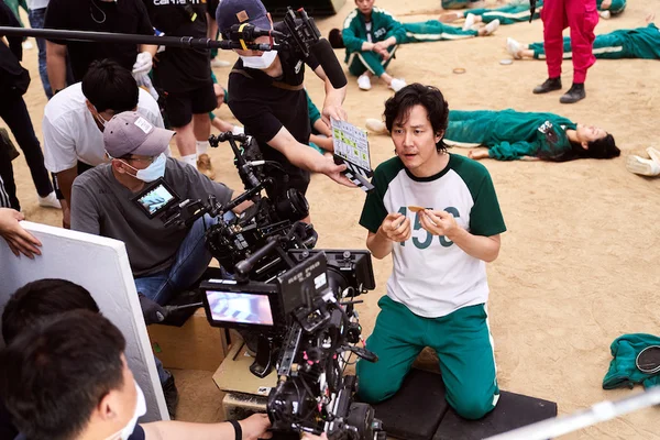 Tournage de Squid Game : un acteur en survêtement vert à genoux sur le sable.