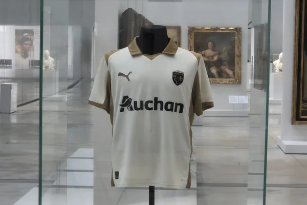 Maillot third du RC Lens exposé dans une vitrine au Louvre-Lens, entouré d'œuvres d'art.