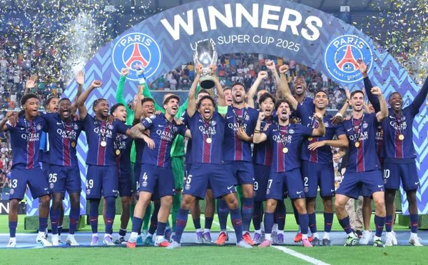 Les joueurs du PSG célèbrent leur victoire en Super Coupe de l'UEFA 2025, trophée levé sous une arche commémorative et des confettis.