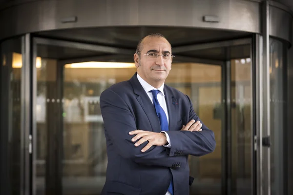 Laurent Nuñez en costume, les bras croisés devant une porte vitrée.
